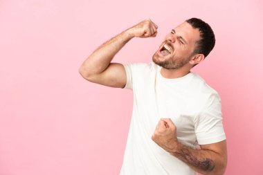 Pembe arka planda izole edilmiş genç Brezilyalı bir adam zaferi kutluyor.