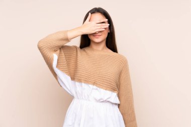 Beyazlı genç bir kadın bej arka planda izole edilmiş, gözleri elle kapatılmış. Bir şey görmek istemiyorum.