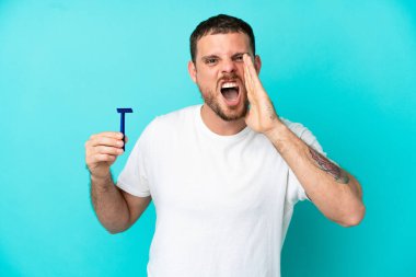 Mavi arka planda sakalını tıraş eden Brezilyalı adam ağzı açık bağırıyor.