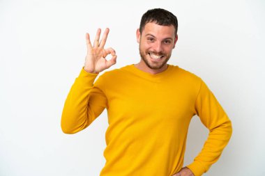 Beyaz arka planda izole edilmiş genç Brezilyalı adam parmaklarıyla tamam işareti gösteriyor