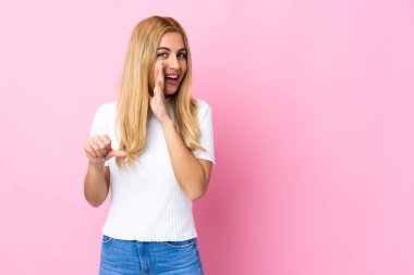 Genç Uruguaylı sarışın kadın pembe arka planda bir ürün sunup bir şeyler fısıldıyor.