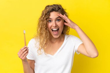 Sarı arka planda dişlerini fırçalayan beyaz bir kadın sürpriz bir ifadeyle izole edilmiş.