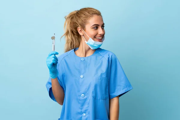 Młoda Kobieta Dentysta Trzyma Narzędzia Odizolowanym Niebieskim Tle Patrząc Boku — Zdjęcie stockowe