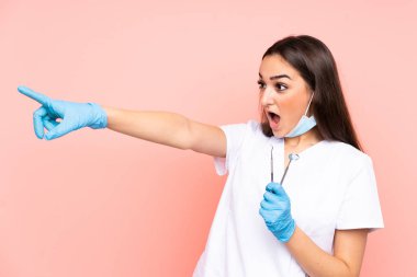 Pembe arka planda izole edilmiş aletleri tutan dişçi kadın.