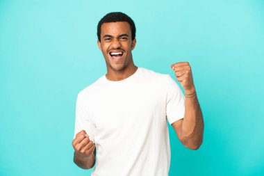 Afro-Amerikalı yakışıklı adam mavi arka planda zaferi kutluyor.