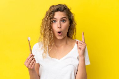 Sarı arka planda dişlerini fırçalayan beyaz bir kadın çözümü bulmak için parmağını kaldırıyor.