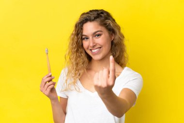 Sarı arka planda dişlerini fırçalayan beyaz bir kadın geliyor.