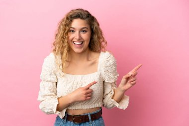 Pembe arka planda izole edilmiş genç sarışın kadın korkmuş ve kenarı işaret ediyor.