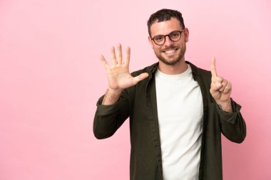 Pembe arka planda izole edilmiş genç Brezilyalı adam parmaklarıyla altısını sayıyor
