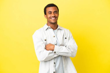 Sarı arka planda kollarını kavuşturup ileriye bakan Afro-Amerikalı yakışıklı bir adam.