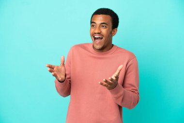 Yüzünde sürpriz bir ifade olan, izole edilmiş mavi arka planda Afro-Amerikalı yakışıklı bir adam.