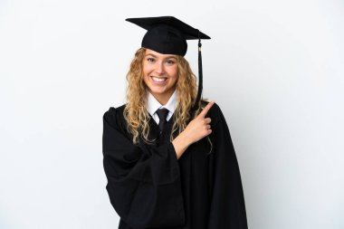 Beyaz arka planda izole edilmiş genç üniversite mezunu bir ürünü sunmak için kenarı işaret ediyor