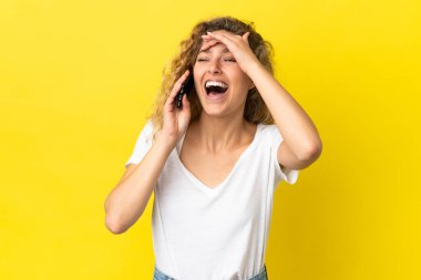 Sarı arka planda izole edilmiş cep telefonu kullanan genç sarışın kadın çok gülümsüyor.