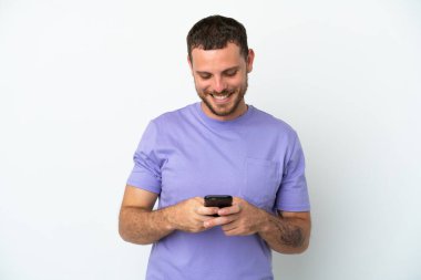 Genç Brezilyalı bir adam beyaz arka planda izole edilmiş cep telefonuyla mesaj gönderiyor.