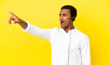 Afrika kökenli Amerikalı bir pazarlamacı, izole edilmiş sarı arka planda kulaklıkla çalışıyor.