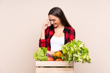 Bej arka planda izole edilmiş bir kutuda taze sebze toplayan çiftçi gülüyor.