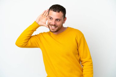 Genç Brezilyalı bir adam beyaz arka planda izole edilmiş bir şekilde elini kulağına koyarak bir şeyler dinliyor.