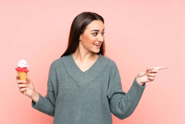 Jonge Vrouw Met Een Cornet Ijs Geïsoleerd Roze Achtergrond Wijzend — Stockfoto