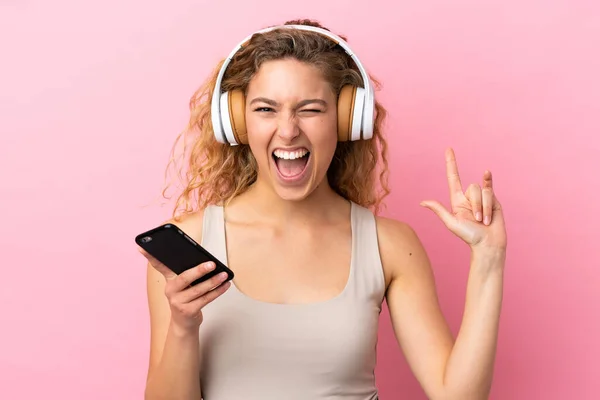 Jovem Loira Isolada Fundo Rosa Ouvindo Música Com Gesto Rock — Fotografia de Stock