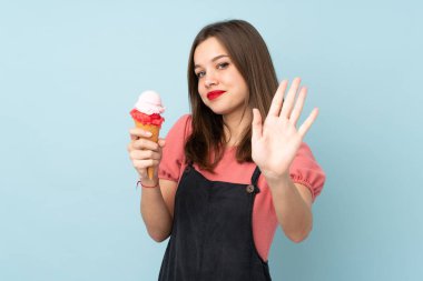 Kornet dondurması tutan genç kız mavi arka planda izole edilmiş mutlu bir ifadeyle selamlıyor.