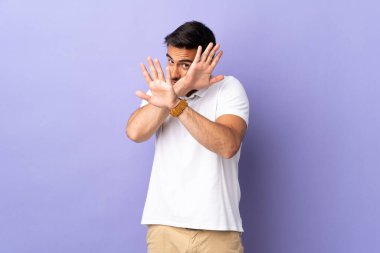 Mor arka planda soyutlanmış genç ve yakışıklı bir adam gergin ellerini öne uzatıyor.