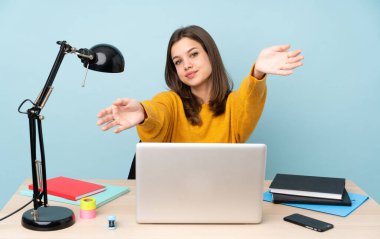 Öğrenci kız evinde çalışıyor. Mavi arka planda izole edilmiş. Sunar ve davet eder.