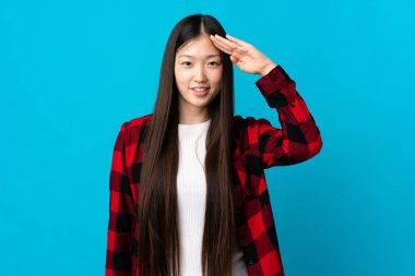 Genç Çinli kız mavi arka planda mutlu bir ifadeyle selamlıyor.