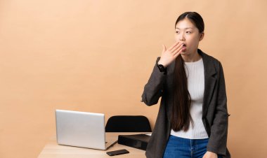 İş yerinde Çinli bir iş kadını esniyor ve ağzı açık bir şekilde elleriyle ağzını kapatıyor.