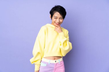 Genç Vietnamlı bir kadın, kısa saçlı, izole edilmiş mor bir geçmişi var, yana bakıyor ve gülümsüyor.