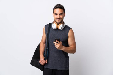 Spor çantalı genç adam beyaz arka planda izole edilmiş cep telefonuyla bir mesaj gönderiyor.