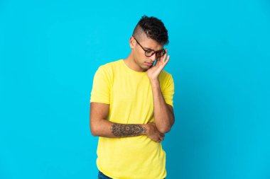 Mavi arka planda baş ağrısı olan genç Brezilyalı bir adam izole edilmiş.