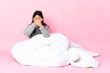 Genç melez kadın pijamasını giymiş yerde oturuyor ve bir hareketi durdurmak için el hareketi yapıyor.