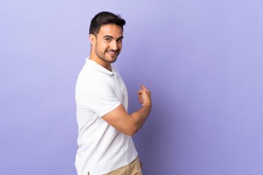 Mor arka planda izole genç yakışıklı adam geriye işaret ediyor