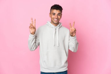 Pembe arka planda izole edilmiş genç Brezilyalı iki eliyle zafer işareti gösteriyor.