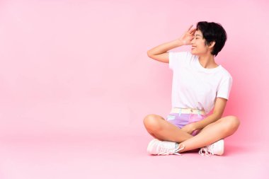 Kısa saçlı genç Vietnamlı kadın pembe arka planda izole bir şekilde otururken bir şey fark etti ve çözüme niyetlendi.