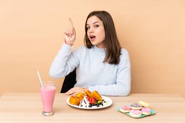 Bej arka planda izole edilmiş waffle yiyen genç kız parmağını kaldırarak çözümü bulmaya çalışıyor.