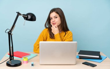 Evinde okuyan öğrenci kız mavi arka planda tek başına gülümsüyor.