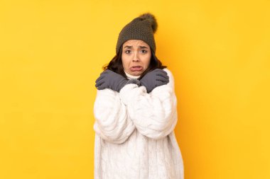 Kışlık şapkalı genç kadın izole edilmiş sarı arka planda donuyor.