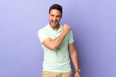 Mor arka planda izole genç yakışıklı bir adam zaferi kutluyor.