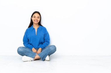 Genç melez kadın beyaz arka planda yapayalnız oturmuş gülüyor.