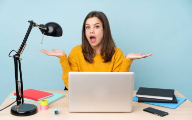 Öğrenci kız evinde çalışıyor. Mavi arka planda, şok olmuş bir yüz ifadesi var.