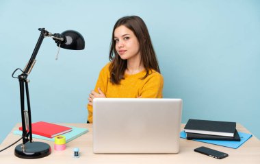 Öğrenci kız evinde çalışıyor. Mavi arka planda izole edilmiş, kolları bağlı ve mutlu.