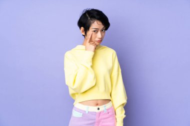 Kısacık saçlı genç Vietnamlı kadın, izole edilmiş mor arka planda bir fikir düşünüyor.