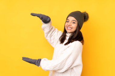 Sarı arka plan üzerinde kışlık şapkalı genç bir kadın ilan vermek için kopyalama alanı tutuyor.