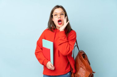 Mavi arka planda kitap tutan öğrenci kız ağzı açık bağırıyor.