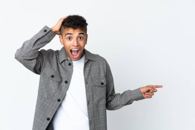 Beyaz arka planda izole edilmiş genç Brezilyalı şaşırmış ve parmağıyla kenarı işaret ediyor.