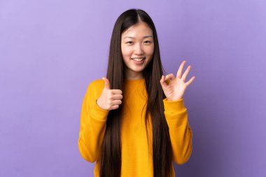 Mor arka planda izole edilmiş genç Çinli kız işaret ve baş parmak işareti gösteriyor.