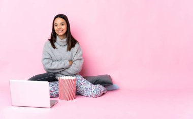 Genç melez kadın dizüstü bilgisayarda film izlerken patlamış mısır yiyor kolları bağlı ve ileriye bakıyor.