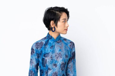 Genç Vietnamlı kadın, kısa saçlı, geleneksel bir elbise giyiyor, izole edilmiş beyaz arka planda, yan tarafa bakıyor.