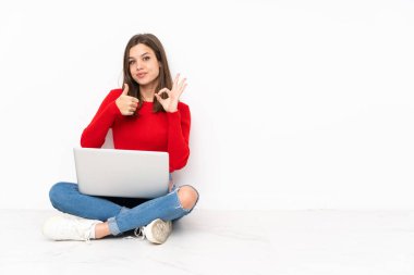 Beyaz arkaplan üzerinde bilgisayar ile çalışan tenaager kız Tamam işareti ve başparmak işareti göstererek jest